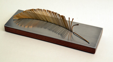 escultura para regalo corporativo que representa una pluma en bronce, madera y aluminio